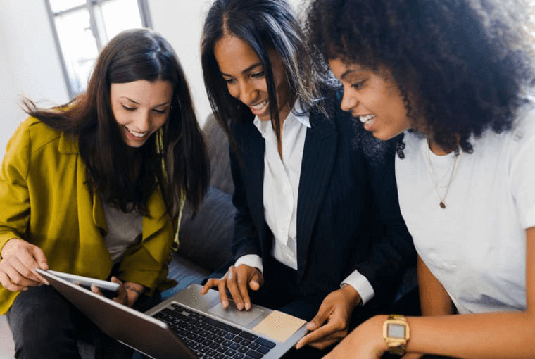 Three business women smiling at a laptop together.