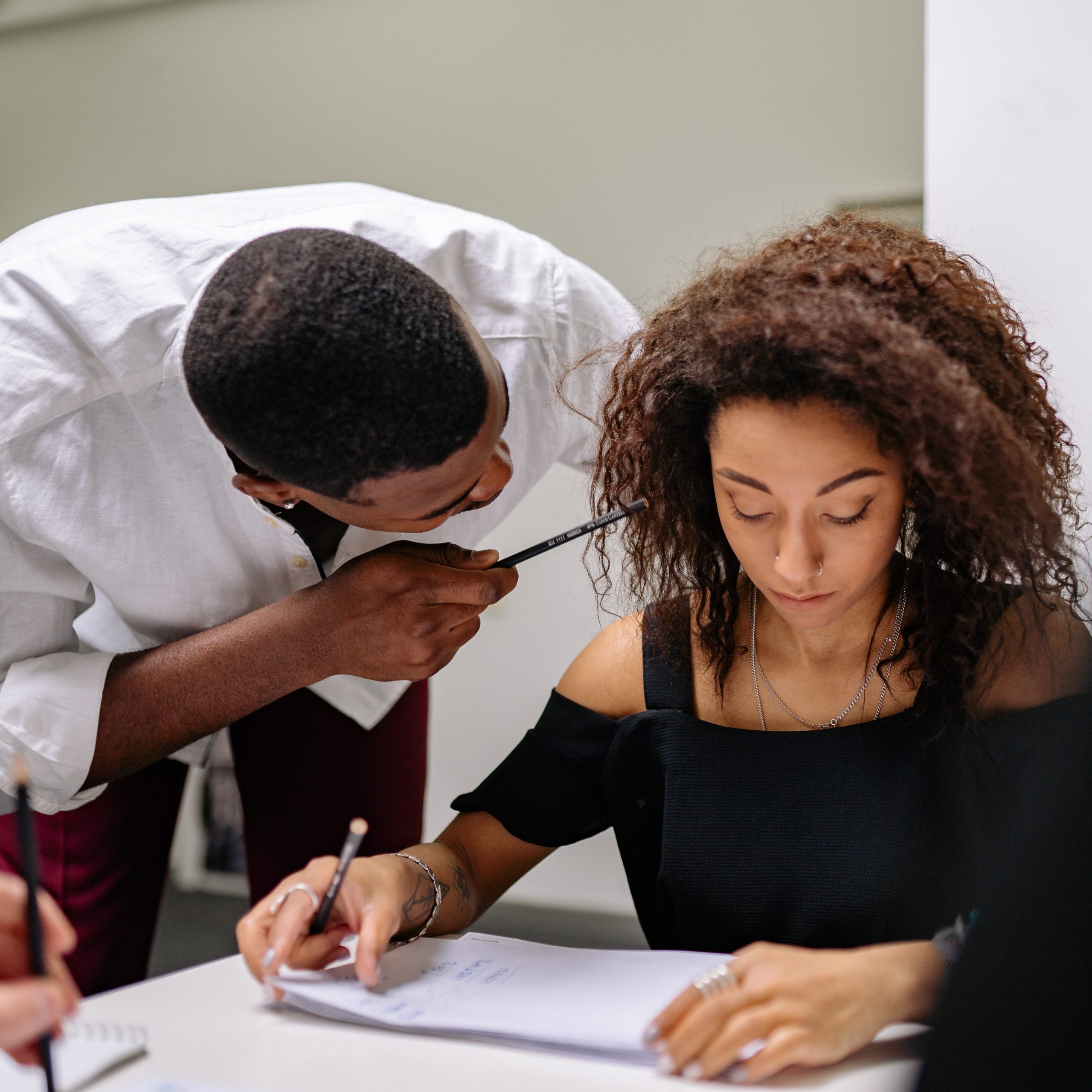 A woman sitting at a desk and a man bent over her looking like he's agressively saying something close to her face
